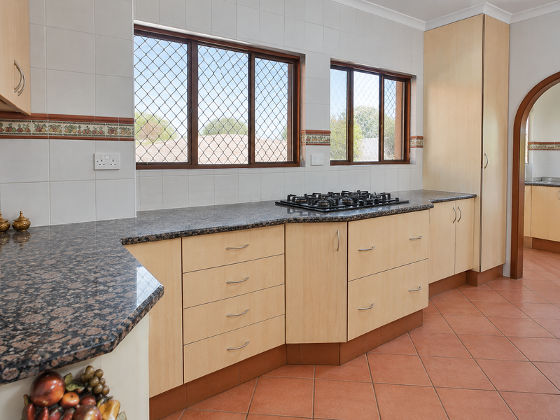 A functional kitchen featuring granite countertops, a gas hob, light wood cabinetry, and tiled flooring, with an arched doorway leading to an adjacent space.