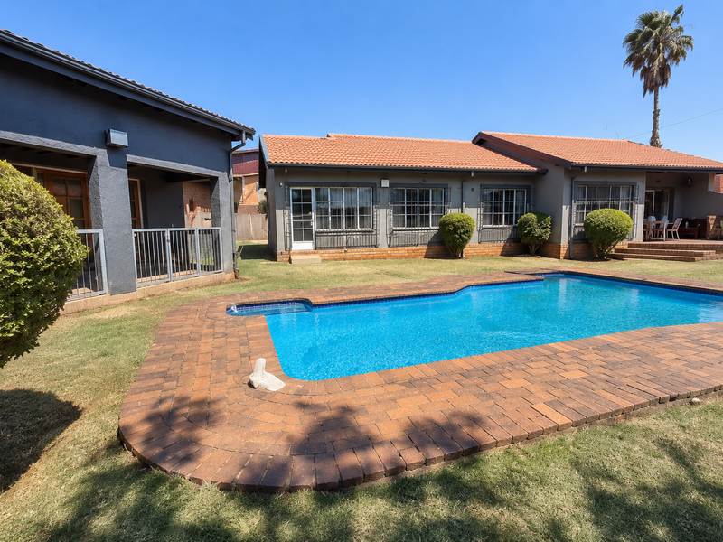 A well-maintained backyard featuring a swimming pool with brick paving, surrounded by a landscaped garden and the rear elevation of the house.