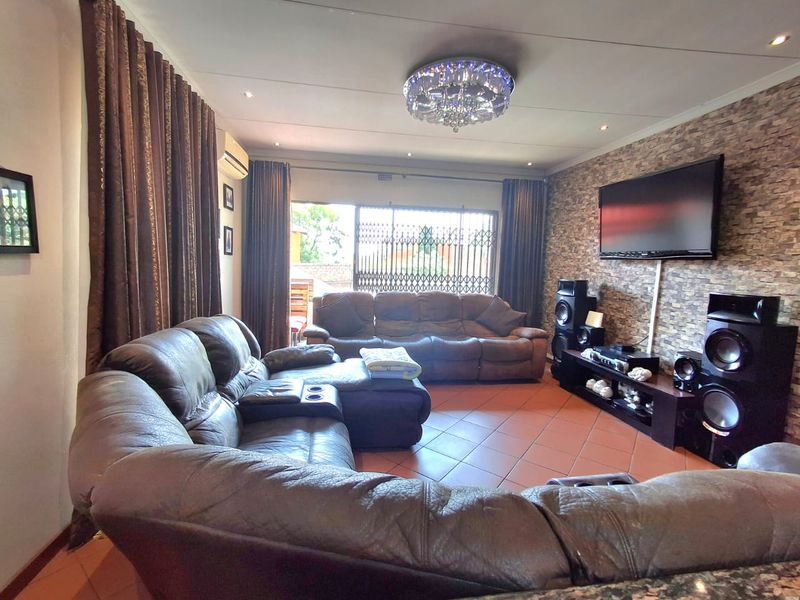 Spacious living room featuring a textured stone-cladding accent wall, tiled flooring, and integrated lighting, providing a comfortable and functional family entertainment space.
