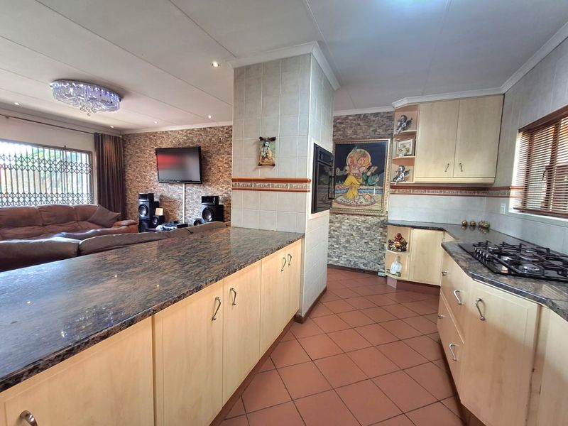 Open-plan kitchen and living area featuring granite countertops, light wood cabinetry, gas hob, built-in oven, and tiled flooring throughout.