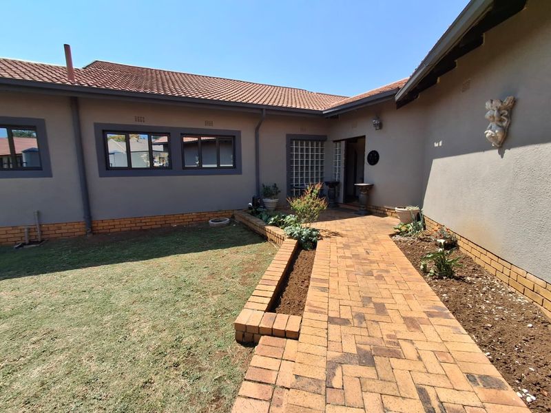 A rear exterior view of the house featuring a brick paved walkway, a built-in brick planter box, and a tiled roof.
