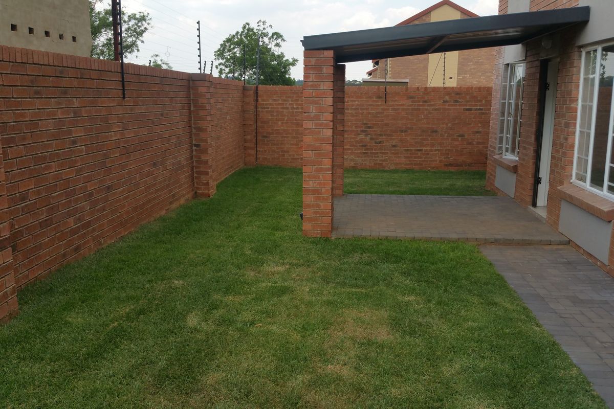 A private rear garden featuring a paved patio area, brick boundary walls, and an established lawn, providing a low-maintenance outdoor space.