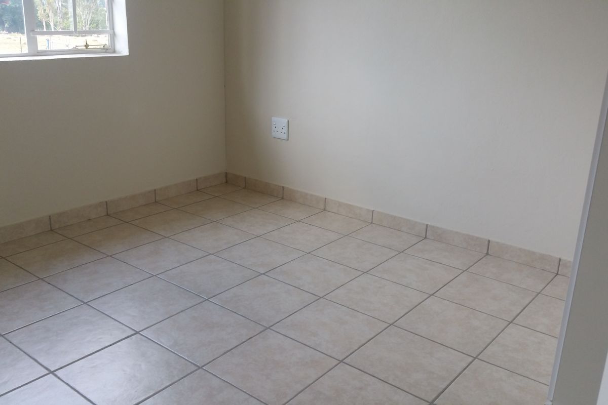 An empty bedroom featuring neutral tiled flooring, matching tiled skirting boards, and a single window providing natural light.