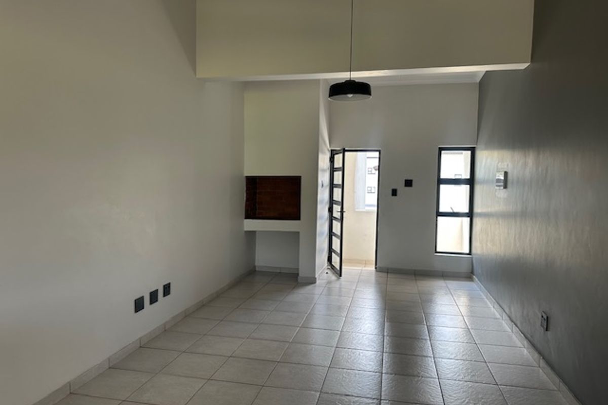 An empty, open-plan living area featuring tiled flooring, a built-in fireplace, and access to an outdoor balcony through a security door.