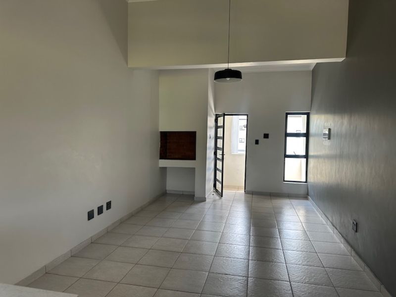 An empty, open-plan living area featuring tiled flooring, a built-in fireplace, and access to an outdoor balcony through a security door.
