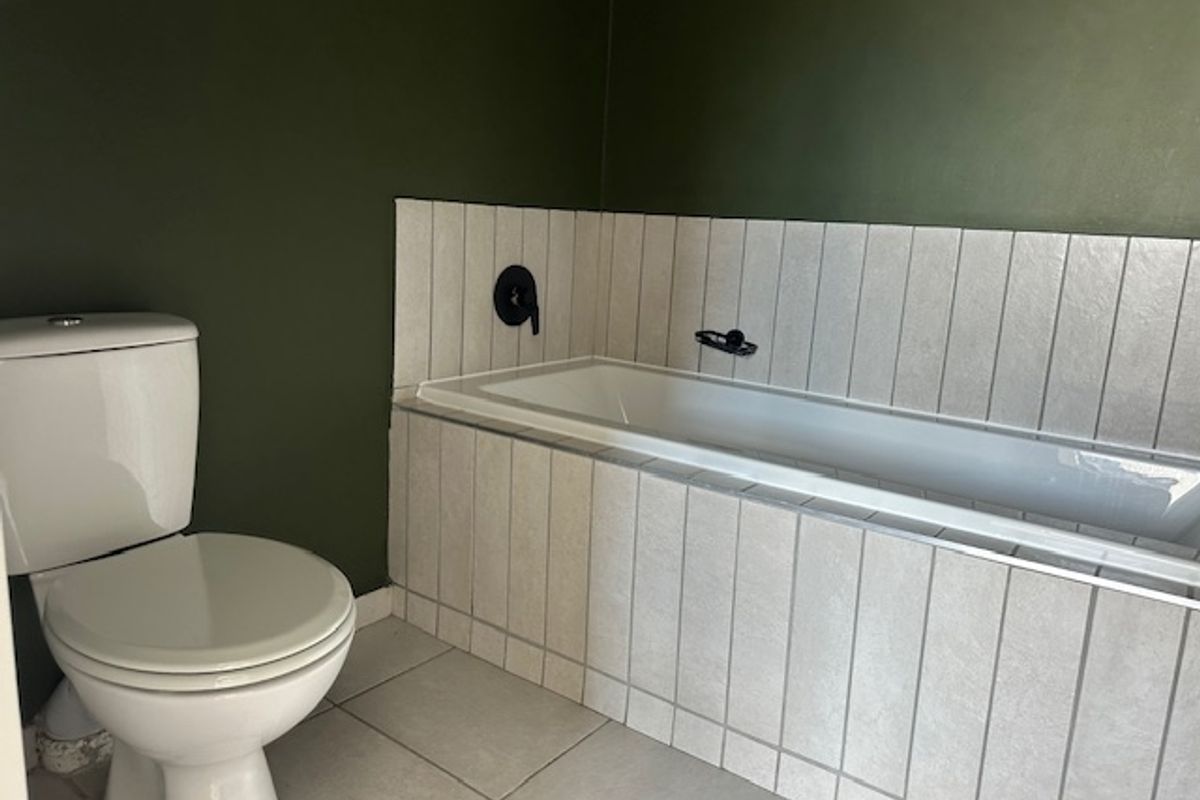A clean bathroom featuring a built-in bathtub with vertical wall tiling, a modern toilet, and dark green painted walls.
