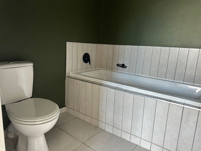 A clean bathroom featuring a built-in bathtub with vertical wall tiling, a modern toilet, and dark green painted walls.