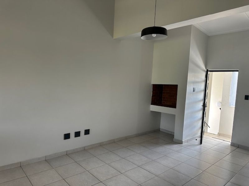 An empty living room featuring tiled flooring, a built-in brick fireplace, and a modern pendant light fixture, leading to an exterior entrance.