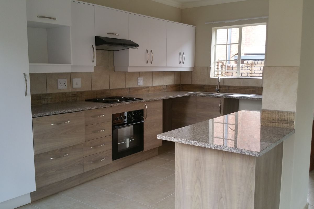 Modern kitchen featuring wood-grain cabinetry, granite countertops, built-in oven, hob, extractor fan, and a breakfast nook, offering a functional and clean workspace.