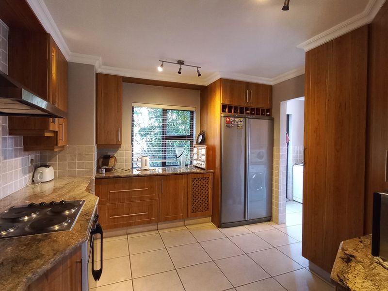 A well-maintained kitchen featuring warm-toned wooden cabinetry, granite countertops, a built-in electric hob, and a tiled backsplash with a functional layout.