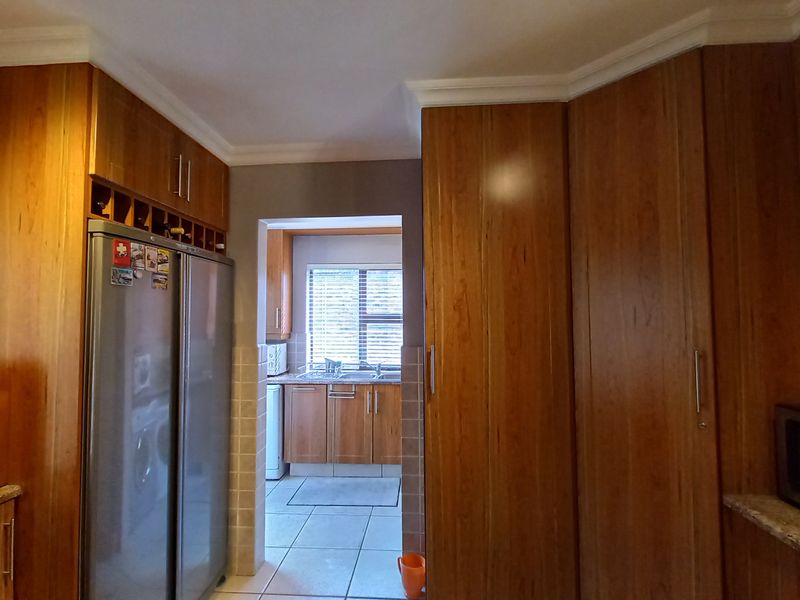A functional kitchen featuring extensive wooden cabinetry, granite countertops, and a separate scullery area with a double sink and tiled flooring.