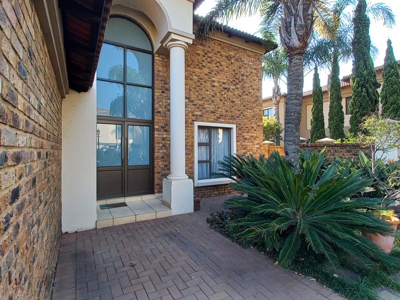 The front entrance features a striking face brick facade, an arched double-volume window, and a paved walkway leading to the main door.