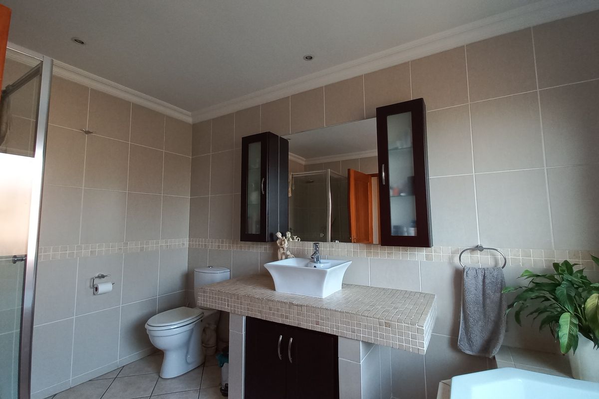 A well-maintained bathroom featuring a vessel sink on a tiled vanity, built-in cabinetry, a shower enclosure, and neutral wall tiling.