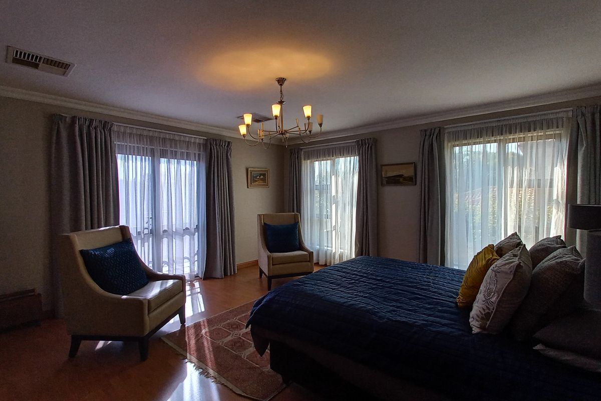 Spacious bedroom featuring hardwood flooring, elegant chandelier lighting, and multiple sliding glass doors providing ample natural light and access to the outdoors.