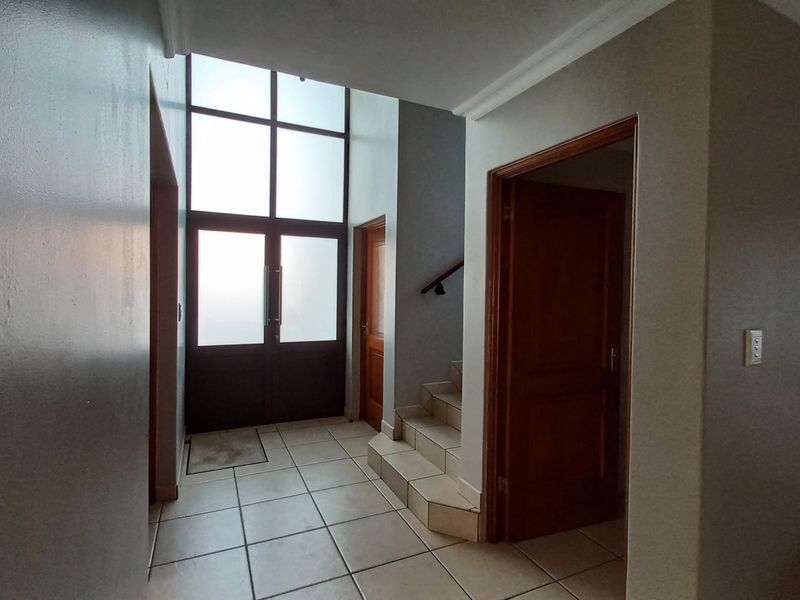 Spacious entrance hall featuring high ceilings, large windows for natural light, tiled flooring, and access to internal rooms and a staircase.