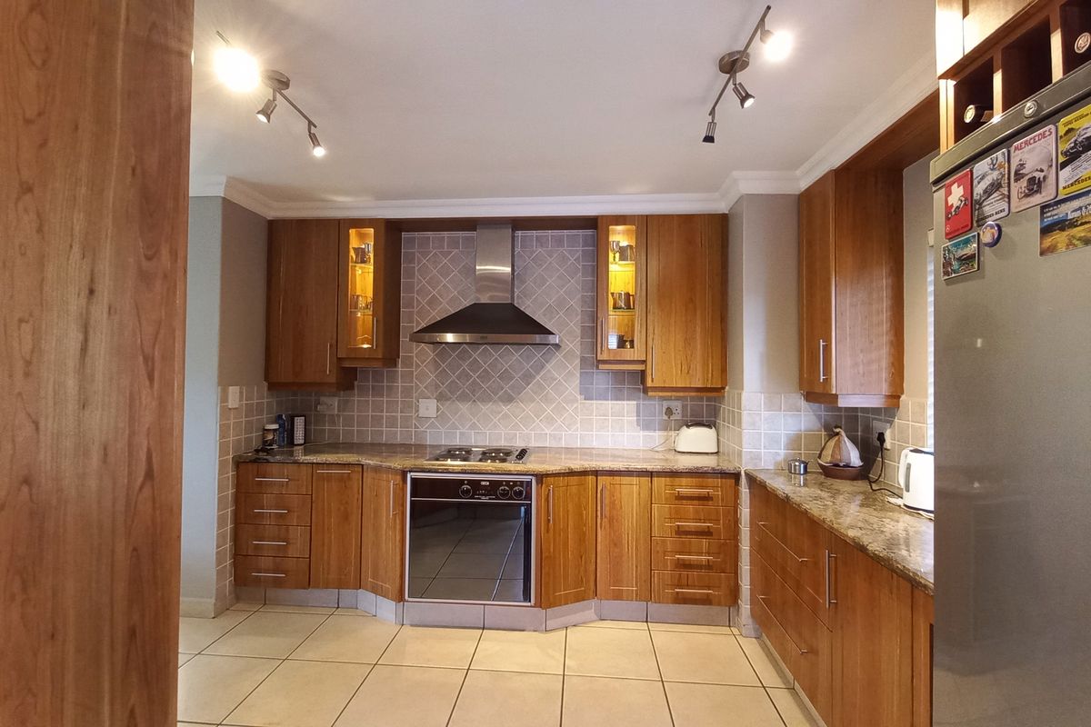 A well-maintained kitchen featuring warm wooden cabinetry, granite countertops, a stainless steel extractor fan, and a built-in oven with a gas hob.