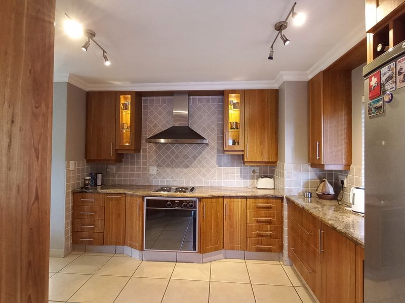A well-maintained kitchen featuring warm wooden cabinetry, granite countertops, a stainless steel extractor fan, and a built-in oven with a gas hob.