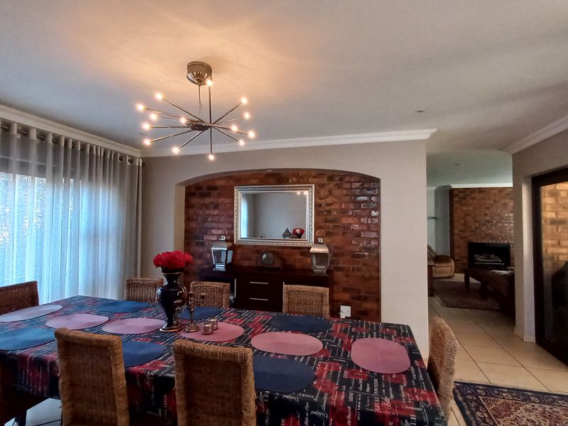 Dining room featuring an exposed brick feature wall with a recessed niche, modern lighting, and tiled flooring, leading into an adjacent living area.