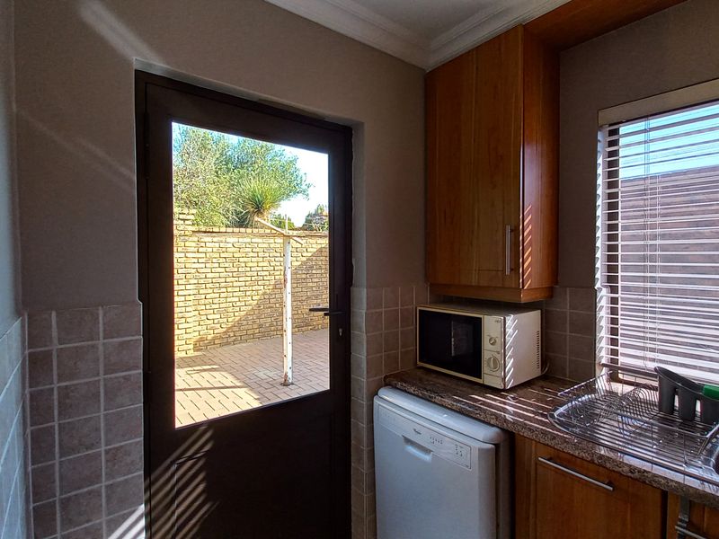 A functional scullery area featuring built-in wooden cabinetry, granite countertops, a stainless steel sink, and direct access to the rear patio.