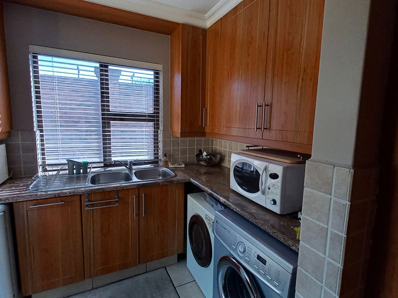 A functional laundry room featuring wooden cabinetry, a double sink, tiled backsplash, and space for under-counter appliances.