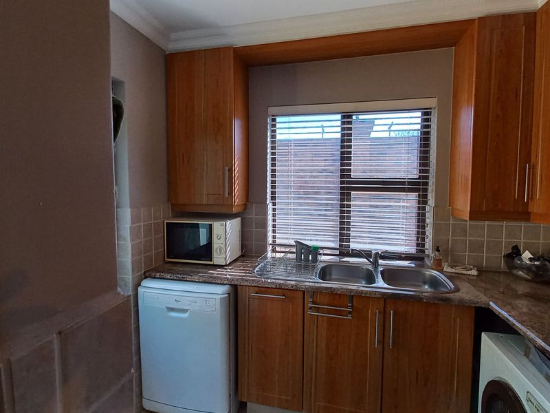 A functional kitchen area featuring wooden cabinetry, a double basin sink, tiled backsplash, and dedicated spaces for under-counter appliances.