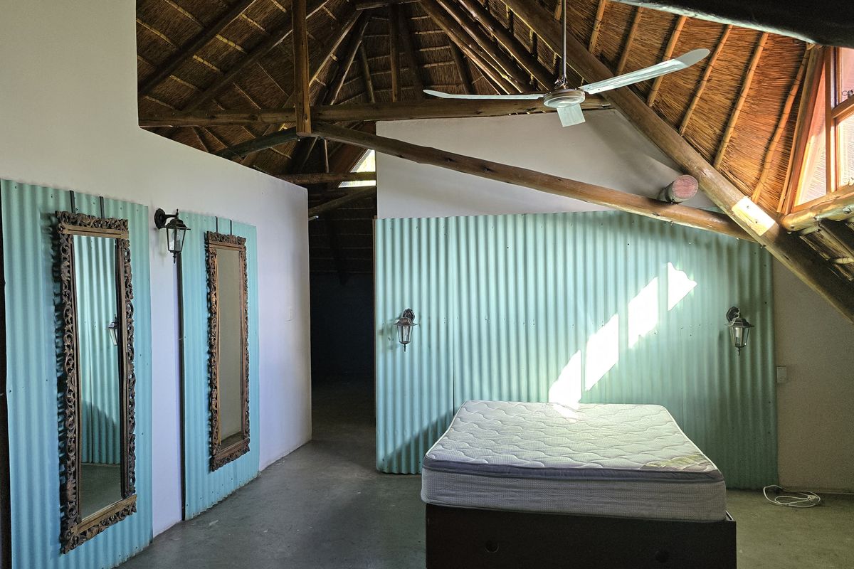 Spacious bedroom featuring a high exposed thatch roof with timber rafters, corrugated metal wall accents, and integrated ceiling fan.