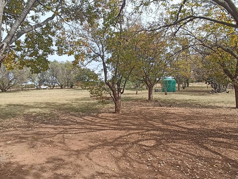 A spacious, tree-lined garden area featuring a water storage tank and perimeter fencing, offering a natural outdoor setting.