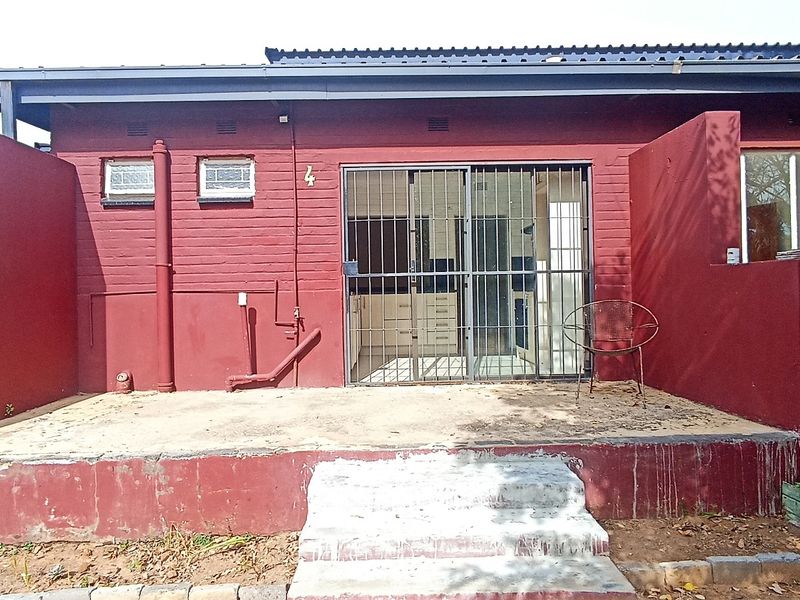 Front exterior view of an apartment unit featuring a red brick facade, concrete patio area, and secure sliding glass entrance.