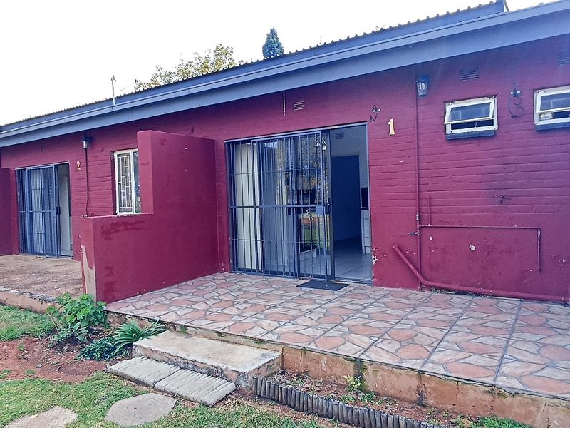 Rear exterior view of apartment units featuring tiled patios, security gates, and brick facade walls showing signs of wear.