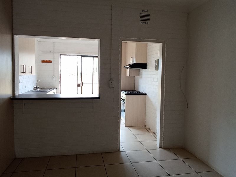 An empty open-plan living area featuring a pass-through kitchen with built-in cabinetry, gas hob, and tiled flooring throughout.