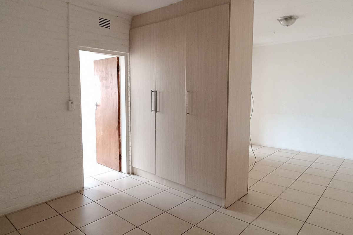 An empty bedroom featuring tiled flooring, built-in cupboards, and a neutral white finish, offering a blank canvas for personalization.