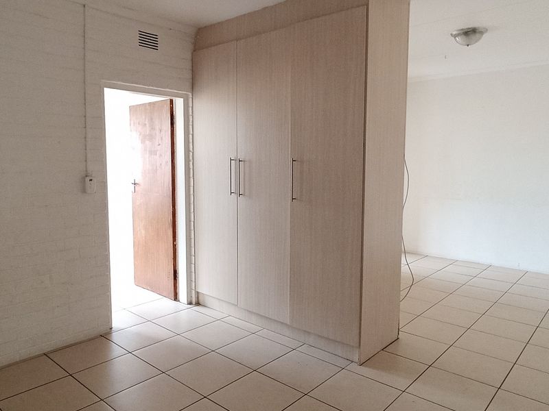 An empty bedroom featuring tiled flooring, built-in cupboards, and a neutral white finish, offering a blank canvas for personalization.