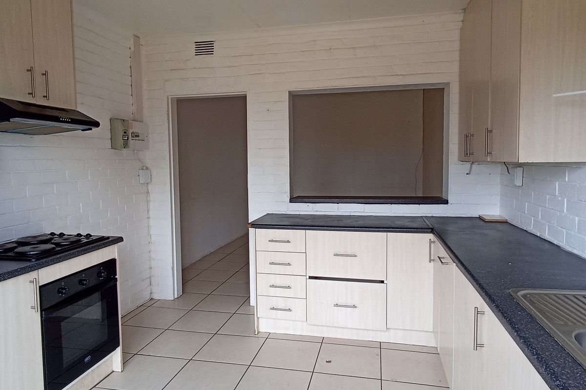 A functional kitchen featuring built-in cabinetry, an electric hob, oven, extractor fan, and a stainless steel sink with tiled flooring.