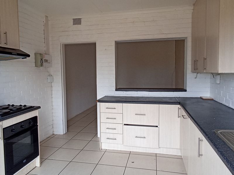 A functional kitchen featuring built-in cabinetry, an electric hob, oven, extractor fan, and a stainless steel sink with tiled flooring.