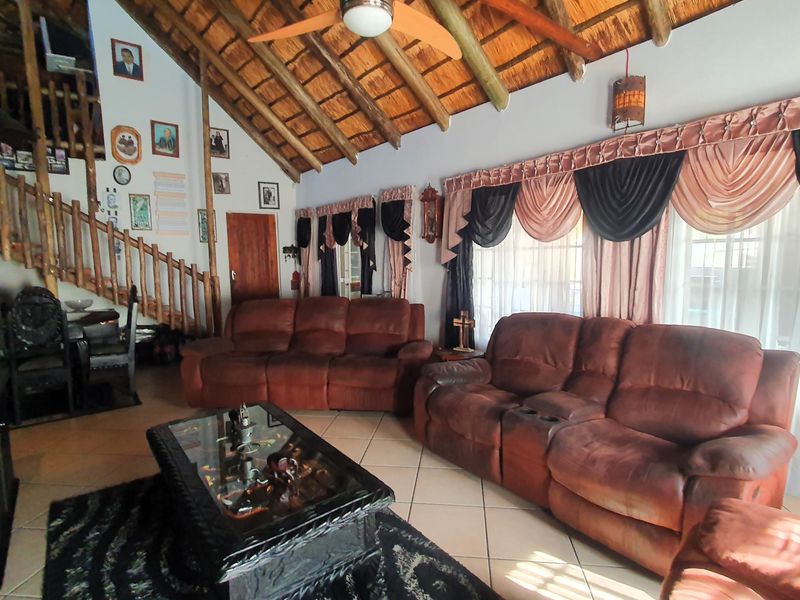 Spacious living room featuring a high vaulted thatched ceiling with exposed timber rafters, ceramic tiled flooring, and a wooden staircase.