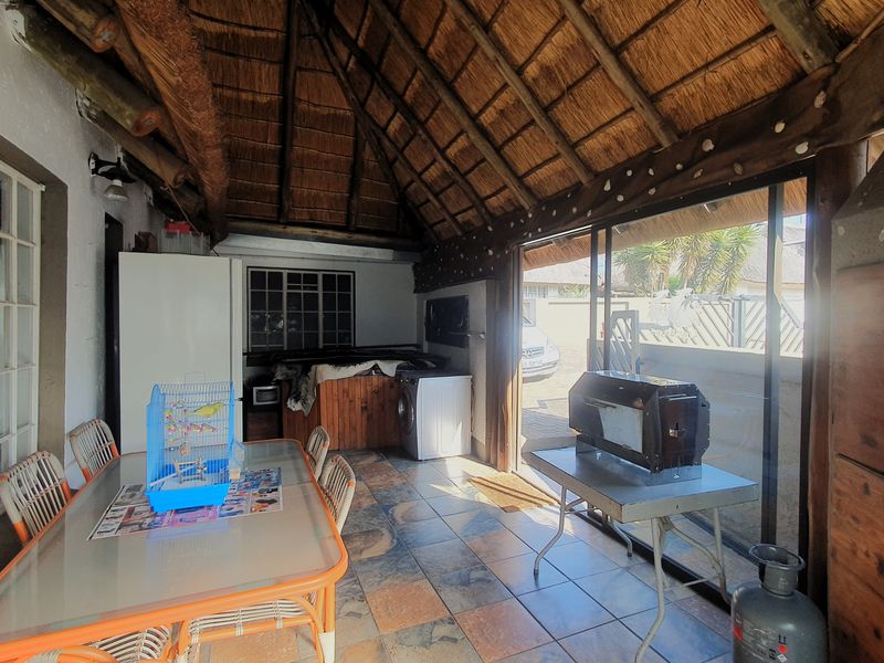 Covered patio area featuring a traditional thatched roof, exposed timber beams, and tiled flooring, providing a versatile outdoor entertainment space.