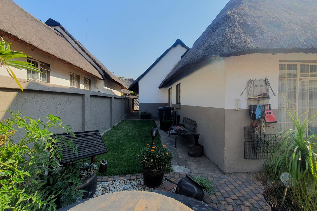 A side garden area featuring a paved walkway, a small lawn, and traditional thatch roof architecture.