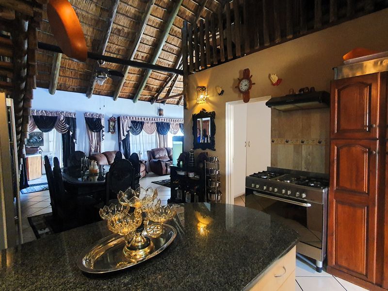 Open-plan living and kitchen area featuring a high thatched ceiling with exposed timber beams, granite island, and gas stove.