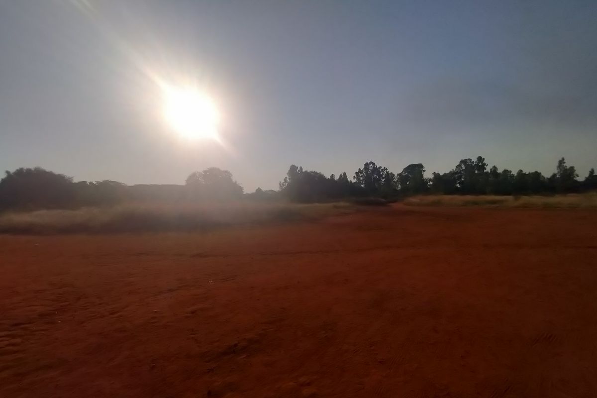 A wide-angle view of a vacant residential plot featuring cleared red earth and surrounding natural vegetation under a bright sky.