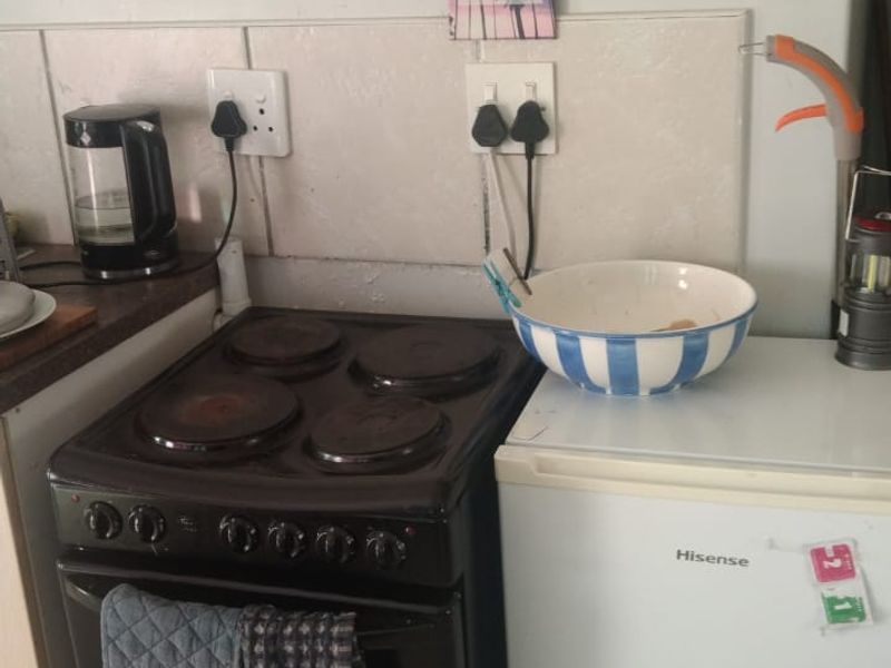 A compact kitchen area featuring a freestanding electric stove and tiled backsplash, requiring some maintenance and cosmetic updates.