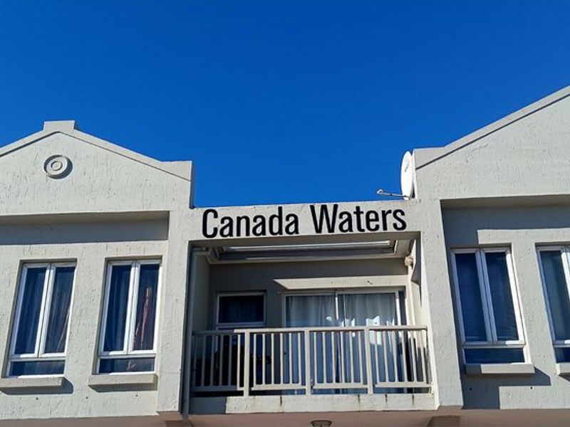 Exterior view of the Canada Waters apartment building facade, featuring a balcony with metal railing and sliding glass doors.