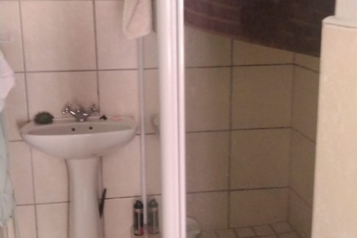 A functional bathroom featuring a pedestal basin, a corner shower enclosure, and neutral wall and floor tiling.