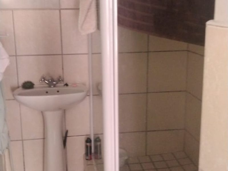 A functional bathroom featuring a pedestal basin, a corner shower enclosure, and neutral wall and floor tiling.