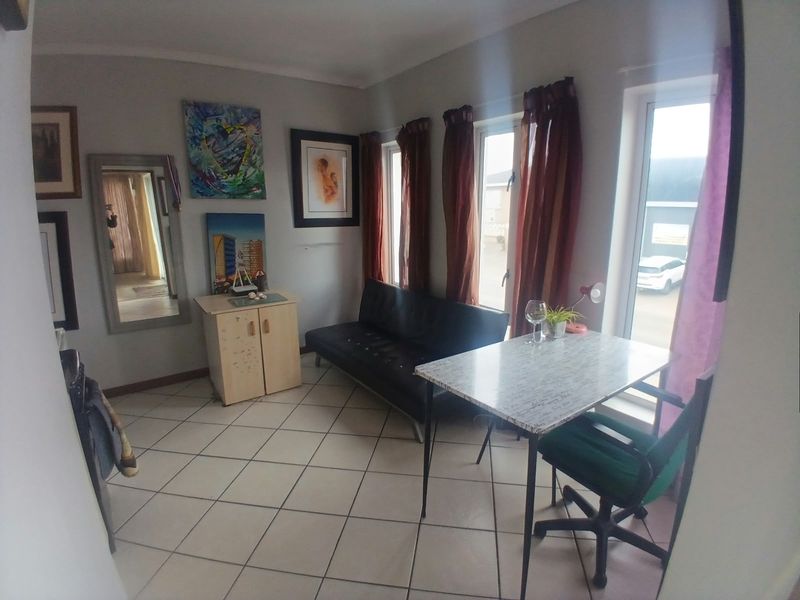 A living area featuring tiled flooring and large windows that provide natural light, offering a functional space for relaxation or dining.