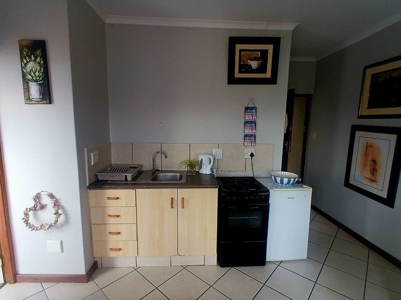 A compact kitchen area featuring built-in cabinetry, a stainless steel sink, tiled backsplash, and a freestanding stove with ceramic floor tiles.