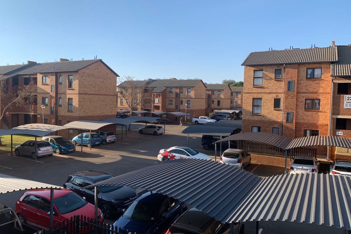 An elevated view of a townhouse complex courtyard featuring multiple brick buildings, covered parking bays, and paved communal areas.