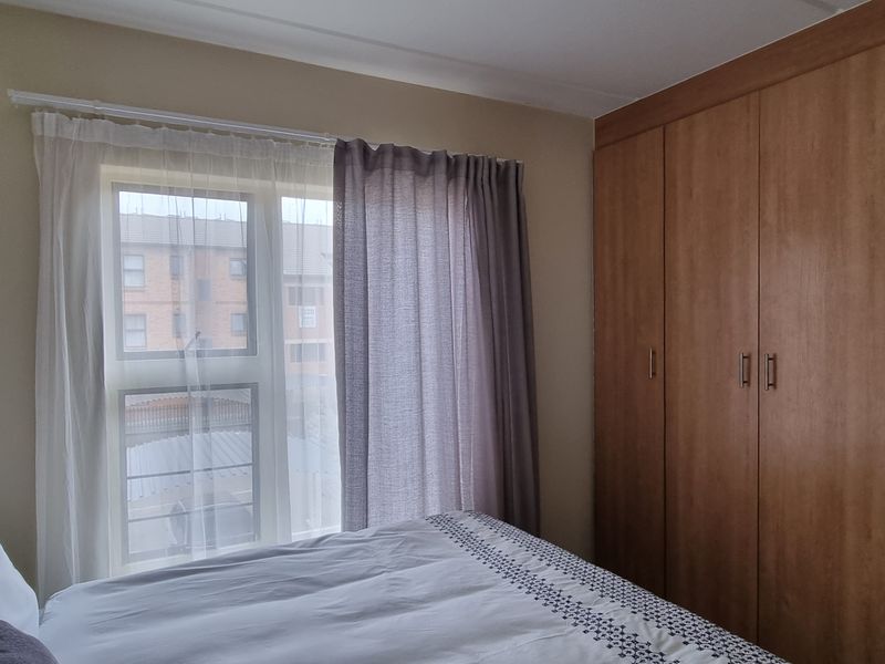 A functional bedroom featuring built-in wooden cupboards and a window with curtain rails, providing natural light and storage space.