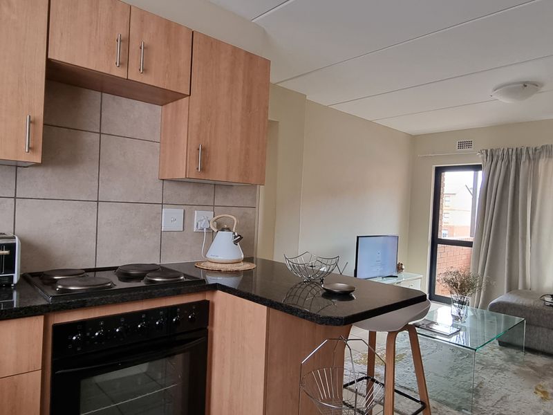 Open-plan kitchen featuring laminate cabinetry, granite countertops, and an integrated electric hob and oven, flowing into a combined living area.