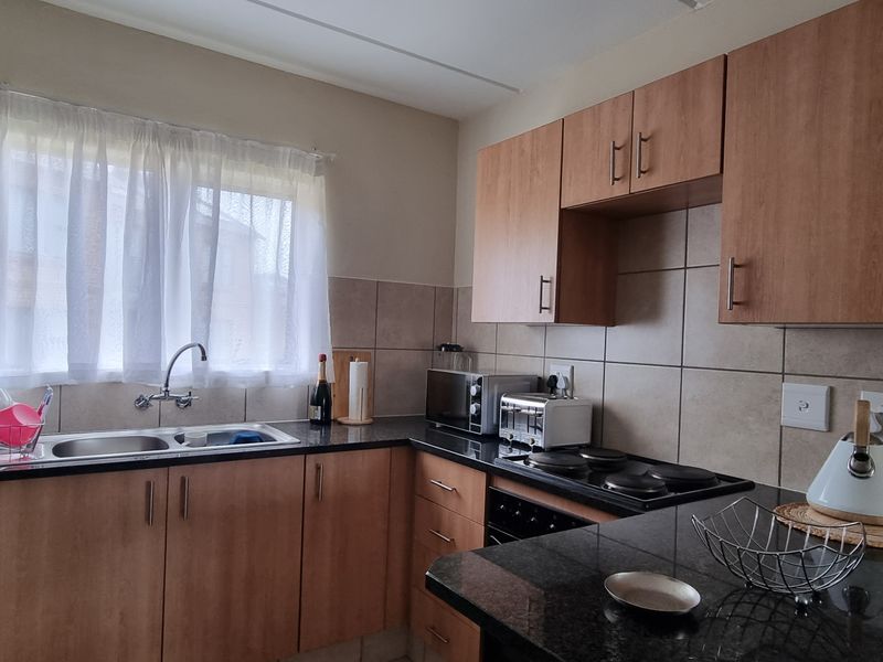 A functional kitchen featuring laminate cabinetry, granite countertops, a double basin sink, and built-in electric cooking appliances with tiled backsplash.