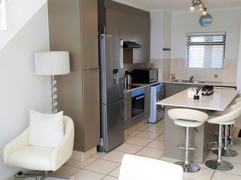 Modern open-plan kitchen featuring sleek cabinetry, a central island with breakfast bar seating, and integrated appliances, seamlessly connected to the living area.